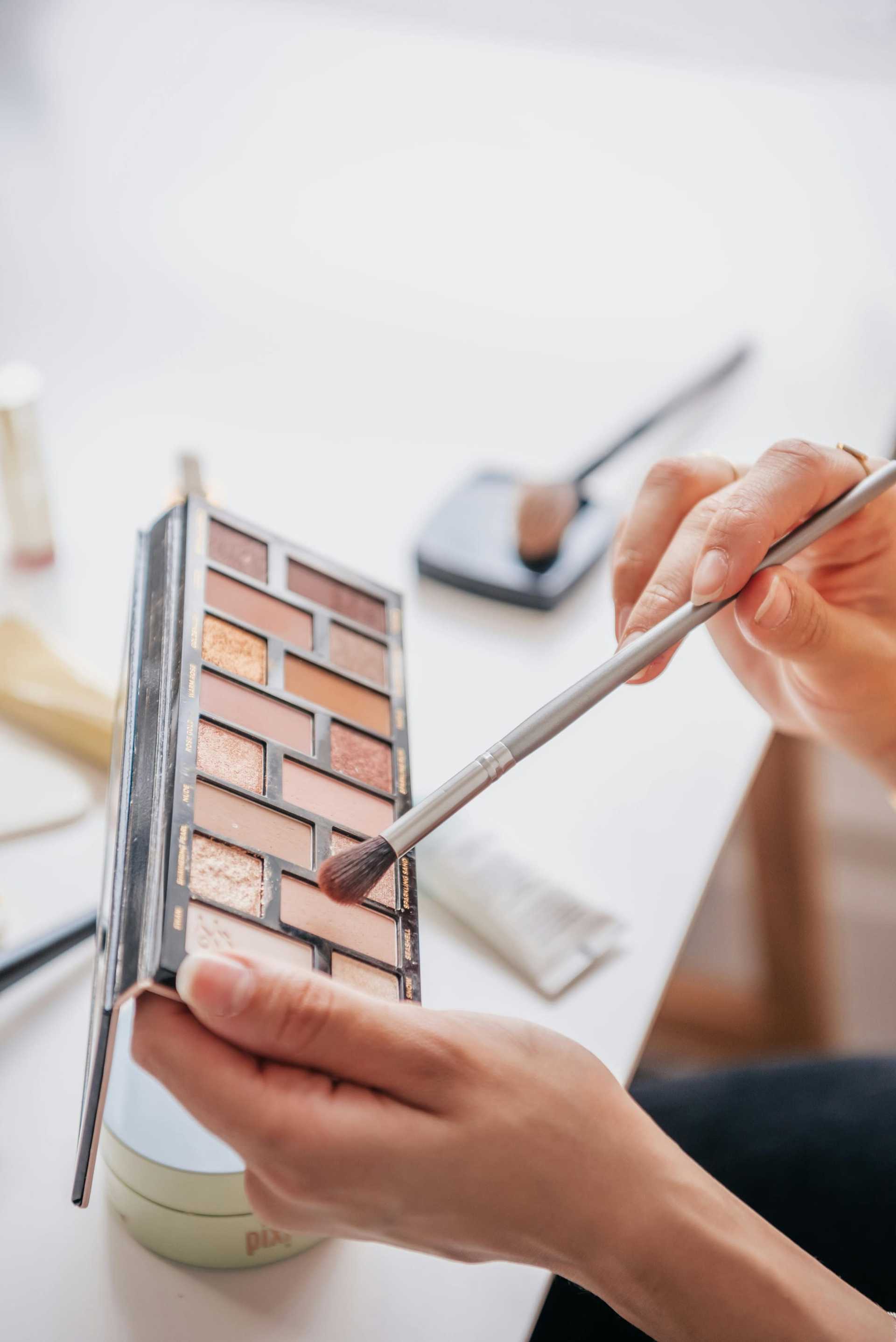 Person applying eyeshadow with a brush from a makeup palette.
