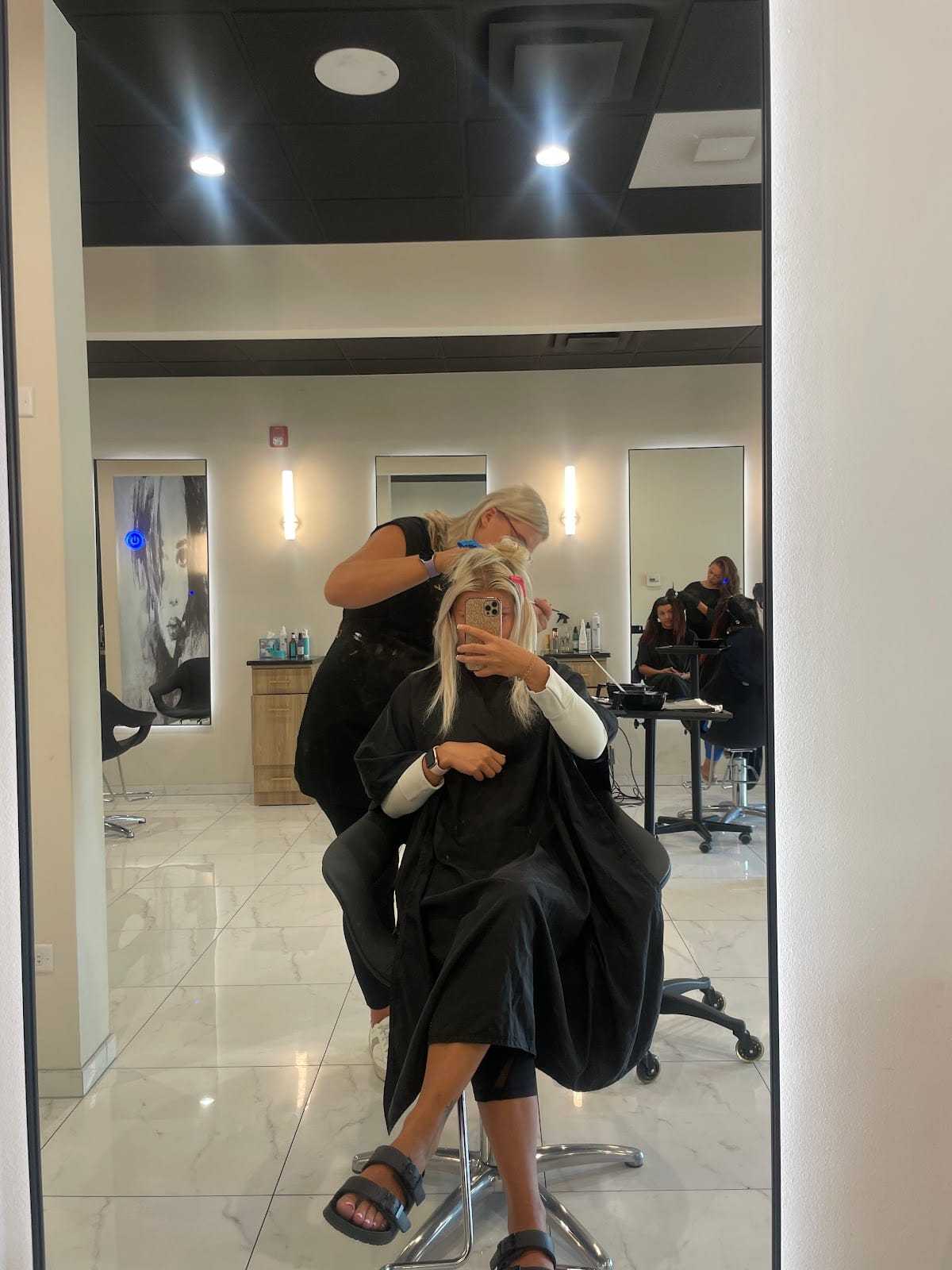 Woman getting her hair styled at a salon with stylist working in the background.