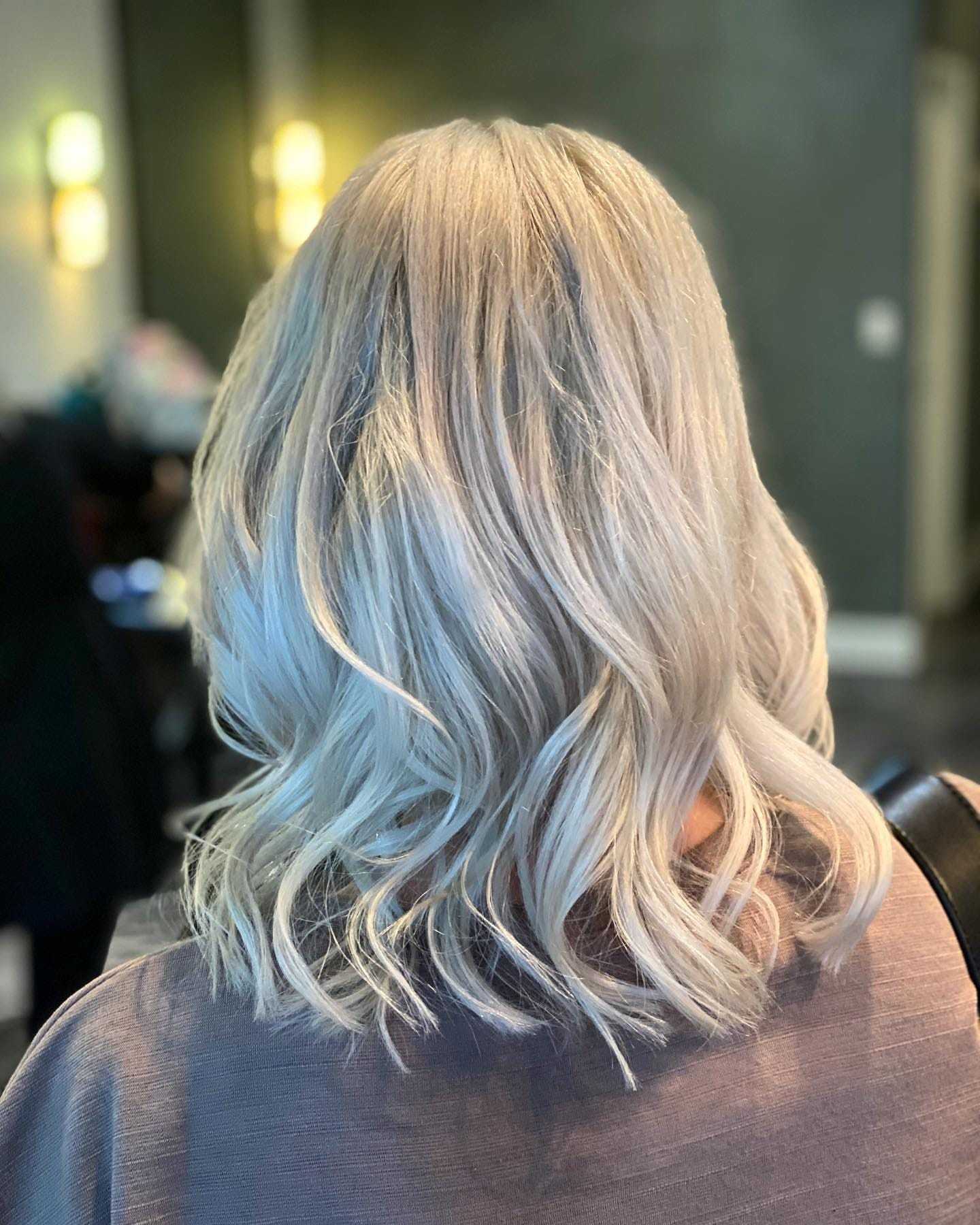 Woman with silver wavy hair seen from the back in a modern indoor setting.